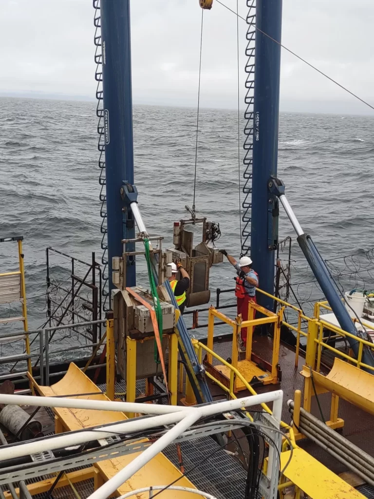 Two men working on the deck of a ship amidst choppy water, engaged in geotechnical field investigation, demonstrating practical application of geotechnical engineering analysis and solutions.