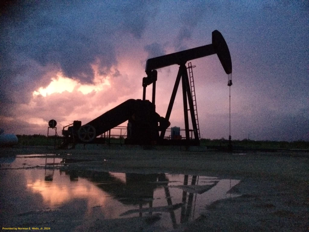 Oil pump jack in the Permian Basin with a colorful sunset reflected in a puddle, symbolizing the integration of archeological investigations and environmental assessments for onshore well permitting in West Texas.